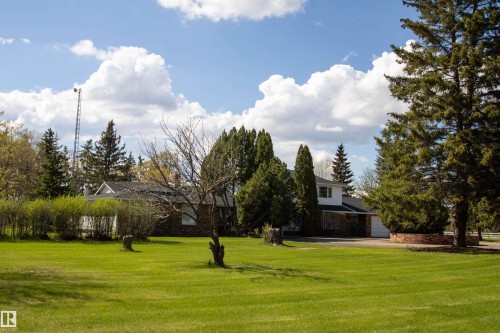 Expansive green lawn with mature trees and a paved driveway leading to a residence featuring a white exterior with brick accents - 58124 Secondary 881, Rural St. Paul County, AB - Outdoor