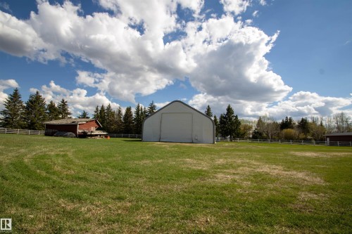 Expansive green space featuring a large quonset-style structure, a rustic red barn, mature evergreen trees, and perimeter fencing - 58124 Secondary 881, Rural St. Paul County, AB - Outdoor