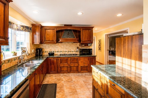 Kitchen featuring wood cabinetry, granite countertops, tile flooring, a tile backsplash, and a built-in range hood - 58124 Secondary 881, Rural St. Paul County, AB - Indoor Photo Showing Kitchen With Double Sink