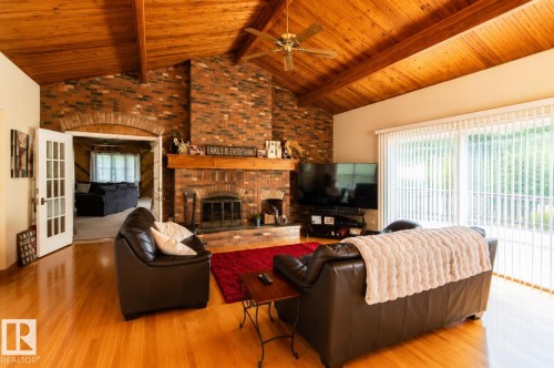 Vaulted wood-paneled ceiling with exposed beams, brick fireplace with wood mantle, hardwood flooring, and sliding glass door to exterior - 58124 Secondary 881, Rural St. Paul County, AB - Indoor Photo Showing Living Room With Fireplace