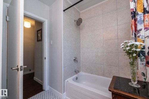 White bathtub with a chrome showerhead, light-toned tile surround, and hexagonal floor tiling - 7719 86 Avenue, Edmonton, AB 