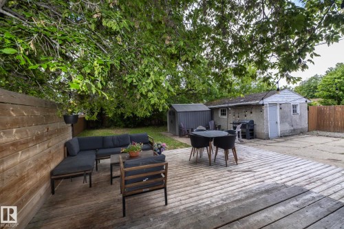 Expansive backyard featuring a large wooden deck, privacy fencing, mature trees providing canopy, a detached storage shed, and a concrete patio - 7719 86 Avenue, Edmonton, AB 