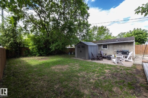 Spacious backyard featuring a concrete patio, a detached storage shed, a stucco-finished building with a window, and a wood fence - 7719 86 Avenue, Edmonton, AB 