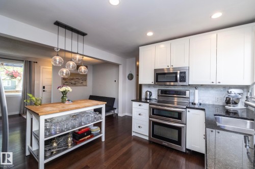 Kitchen featuring dark wood-finish flooring, white cabinetry, dark countertops, and a white subway tile backsplash - 7719 86 Avenue, Edmonton, AB 