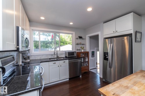 Kitchen featuring white cabinetry, dark stone countertops, stainless steel appliances, and wood-finish flooring - 7719 86 Avenue, Edmonton, AB 