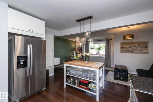 Kitchen featuring white shaker cabinetry, stainless steel refrigerator, dark wood-finish flooring, and a central island with a butcher block countertop - 7719 86 Avenue, Edmonton, AB 