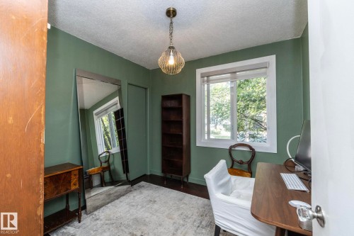 Room featuring a window with white trim, green walls, wood-finish flooring, and a ceiling-mounted light fixture - 7719 86 Avenue, Edmonton, AB 