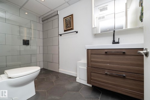 Modern bathroom featuring hexagonal floor tiling, a floating wood-finish vanity with an integrated sink, and a glass-enclosed shower with subway tile surround - 7719 86 Avenue, Edmonton, AB 