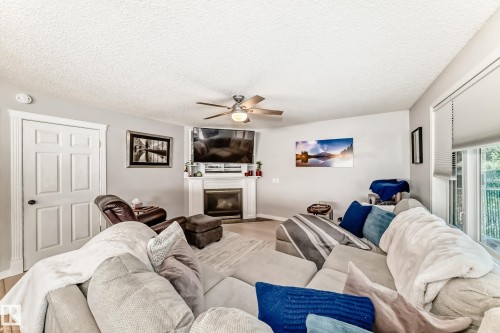 Living area featuring a corner fireplace with white mantel, a ceiling fan with integrated lighting, and light-toned walls - 13 Orchid Place, St. Albert, AB 