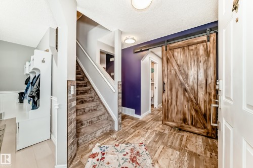 Front entry featuring wood-finish flooring, a barn door, and a staircase with carpeted treads - 13 Orchid Place, St. Albert, AB 