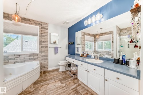 Bathroom featuring a corner jetted tub, wood-finish flooring, and a vanity with an integrated sink and white cabinetry - 13 Orchid Place, St. Albert, AB 