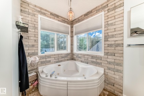 Corner jetted tub with brick-finish accent walls, two windows with blinds, and wood-finish flooring - 13 Orchid Place, St. Albert, AB 