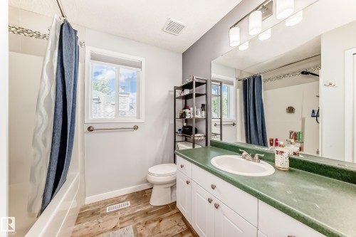 Bathroom featuring a white bathtub with a tiled surround, a white window with a towel bar below, and wood-finish flooring - 13 Orchid Place, St. Albert, AB 