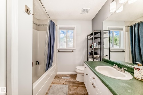 Bathroom featuring a vanity with a green countertop and integrated sink, wood-finish flooring, and a shower-over-tub combination with tiled surround - 13 Orchid Place, St. Albert, AB 