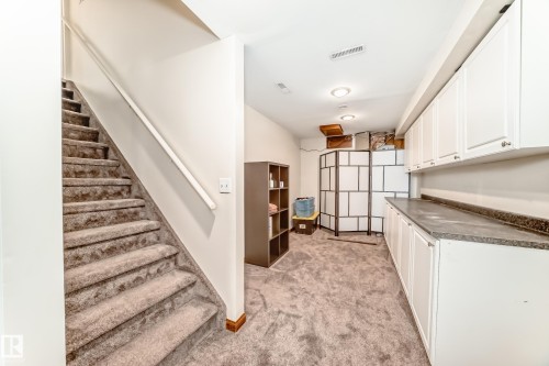 Carpeted staircase with white handrail leading to a finished lower level featuring recessed lighting, extensive white cabinetry with dark countertops, and light-toned wall finishes - 13 Orchid Place, St. Albert, AB 