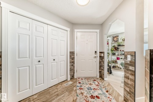 Entryway featuring a white paneled door, wood-finish flooring, and bi-fold closet doors with dark hardware - 13 Orchid Place, St. Albert, AB 