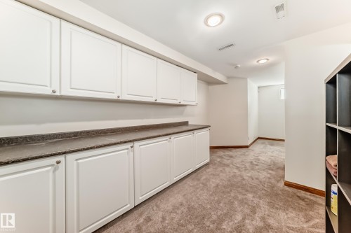 Extensive white cabinetry with silver hardware, dark stone-finish countertops, recessed lighting, and soft carpet flooring throughout - 13 Orchid Place, St. Albert, AB 