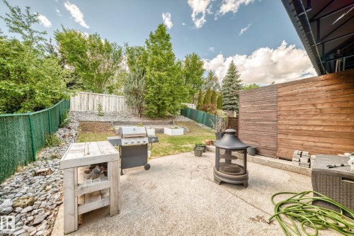 Concrete patio with perimeter landscaping, featuring a wooden privacy fence, mature trees, and a sloped terrain - 13 Orchid Place, St. Albert, AB 