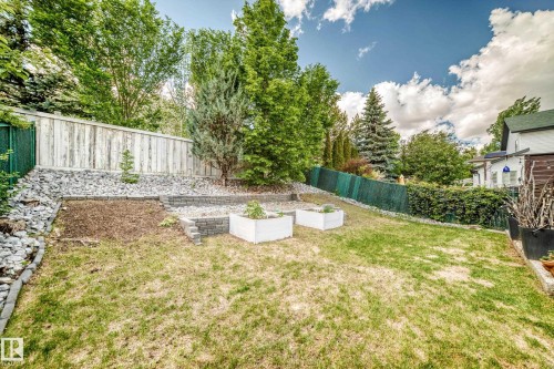 Spacious backyard featuring a sloped lawn, retaining walls, and two raised garden beds - 13 Orchid Place, St. Albert, AB 