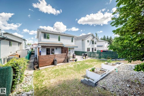 Rear exterior featuring a ground-level patio, privacy fencing, and raised garden beds - 13 Orchid Place, St. Albert, AB 
