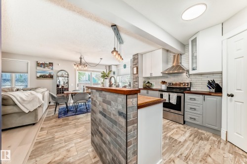 Open-concept living space featuring wood-finish flooring, a kitchen island with stone tile accent, stainless steel appliances, white subway tile backsplash, and wood countertops - 13 Orchid Place, St. Albert, AB 
