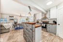 Open-concept living space featuring wood-finish flooring, a kitchen island with stone tile accent, stainless steel appliances, white subway tile backsplash, and wood countertops - 13 Orchid Place, St. Albert, AB 