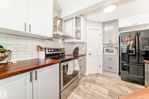 Kitchen featuring wood-finish countertops, subway tile backsplash, stainless steel appliances, and two-tone cabinetry - 13 Orchid Place, St. Albert, AB 