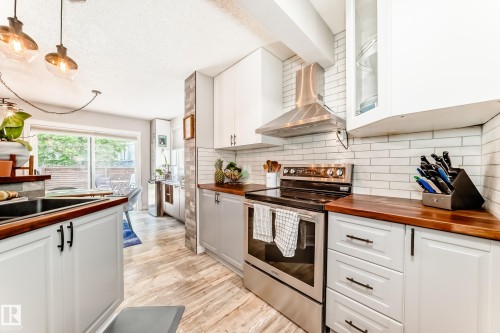 Modern kitchen featuring white shaker-style cabinetry, wood-finish countertops, subway tile backsplash, stainless steel appliances, and wood-look flooring - 13 Orchid Place, St. Albert, AB 