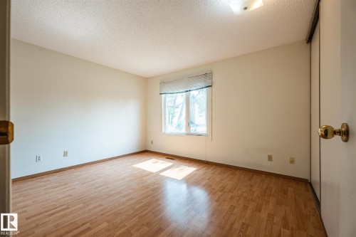 Room featuring wood-finish flooring, a window with horizontal blinds, and a built-in closet with sliding doors - 20 11115 27 Avenue, Edmonton, AB 