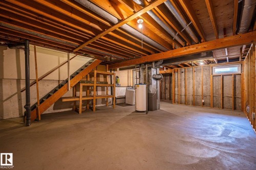 Unfinished basement offering exposed wood joists and structural beams, concrete flooring, and a visible wood-frame staircase - 20 11115 27 Avenue, Edmonton, AB 