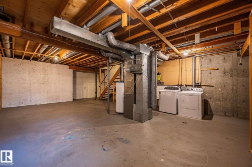 Full unfinished basement featuring exposed wood joists, concrete walls, concrete flooring, and a dedicated laundry area with appliances - 20 11115 27 Avenue, Edmonton, AB 