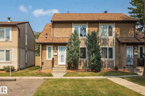 Exterior featuring a brown shingle roof, light brown stucco siding, and a white front entry door with a storm door - 20 11115 27 Avenue, Edmonton, AB 