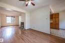 Open-concept living space featuring wood-finish flooring, a ceiling fan with integrated lighting, and a built-in fireplace with a stone hearth - 20 11115 27 Avenue, Edmonton, AB 