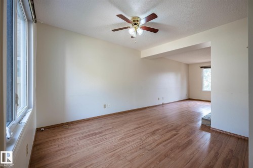 Spacious room featuring wood-finish flooring, a ceiling fan with integrated lighting, and multiple windows providing natural light - 20 11115 27 Avenue, Edmonton, AB 