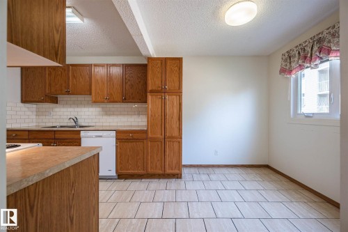Kitchen space featuring wood-finish cabinetry, a white subway tile backsplash, and a double basin sink - 20 11115 27 Avenue, Edmonton, AB 