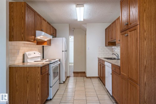 Galley kitchen featuring wood-finish cabinetry, tile flooring, and white subway tile backsplash - 20 11115 27 Avenue, Edmonton, AB 