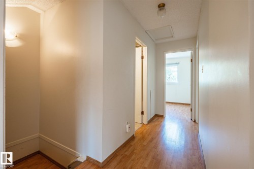 Hallway featuring wood-finish flooring, light-colored walls, and a textured ceiling - 20 11115 27 Avenue, Edmonton, AB 