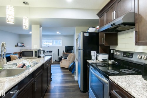 Kitchen featuring dark wood cabinetry, granite-style countertops, stainless steel appliances, and wood-finish flooring - 4004 88 Street, Edmonton, AB 