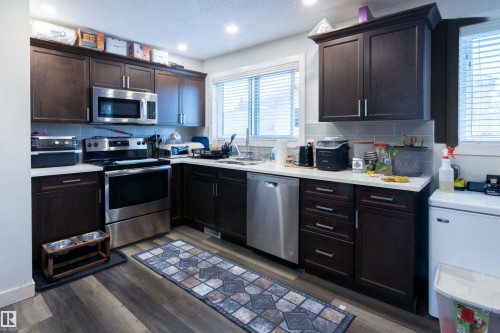 Kitchen featuring dark wood cabinetry, stainless steel appliances, light countertops, and a subway tile backsplash - 4004 88 Street, Edmonton, AB 