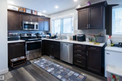 Kitchen featuring dark wood cabinetry, stainless steel appliances, light countertops, and a subway tile backsplash - 