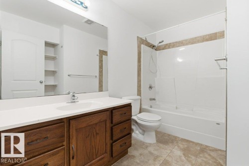 Bathroom featuring a wood-finish vanity with a white countertop and integrated sink, a large wall-mounted mirror, a tub/shower combination with a tiled surround accent, and stone-finish floor tiling - 13279 47 Street, Edmonton, AB - Indoor Photo Showing Bathroom
