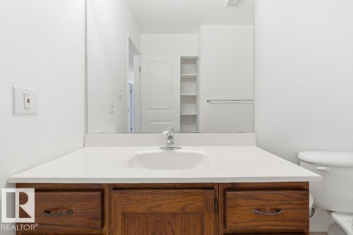 Bathroom vanity featuring a wood-finish cabinet, white countertop, and integrated sink - 13279 47 Street, Edmonton, AB - Indoor Photo Showing Bathroom