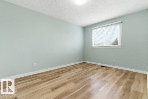 Light wood-finish flooring complements the pastel wall color in this room featuring a window with white blinds, white baseboards, and a flush-mount ceiling light fixture - 13279 47 Street, Edmonton, AB - Indoor Photo Showing Other Room