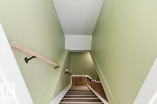 Staircase featuring wood-finish treads, light green painted walls, white trim, and a natural wood handrail with black brackets - 13279 47 Street, Edmonton, AB - Indoor Photo Showing Other Room