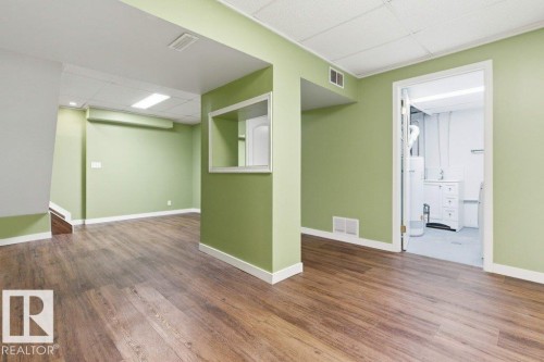 Finished basement room featuring wood-finish flooring, drop ceiling with fluorescent lighting, and a pass-through window - 13279 47 Street, Edmonton, AB - Indoor