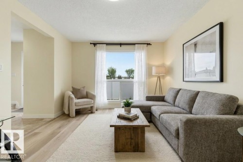 Light-filled living area featuring wood-finish flooring, neutral wall tones, a large picture window with privacy glass, and a wide entryway - 13279 47 Street, Edmonton, AB - Indoor Photo Showing Living Room
