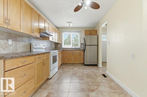Bright kitchen featuring extensive light wood cabinetry, a tiled backsplash, and stone-look countertops - 13279 47 Street, Edmonton, AB - Indoor Photo Showing Kitchen