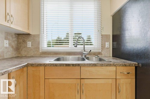 Kitchen featuring a dual-basin stainless steel sink with a chrome faucet, light wood cabinetry, and a mottled countertop - 13279 47 Street, Edmonton, AB - Indoor Photo Showing Kitchen With Double Sink