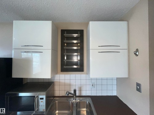 White upper cabinetry with minimalist hardware, stainless steel double basin sink, white subway tile backsplash, and dark countertop - 306 11340 124, Edmonton, AB 