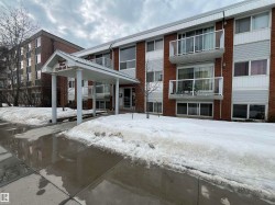 Multi-story brick building featuring white siding accents and a covered entrance with support columns - 